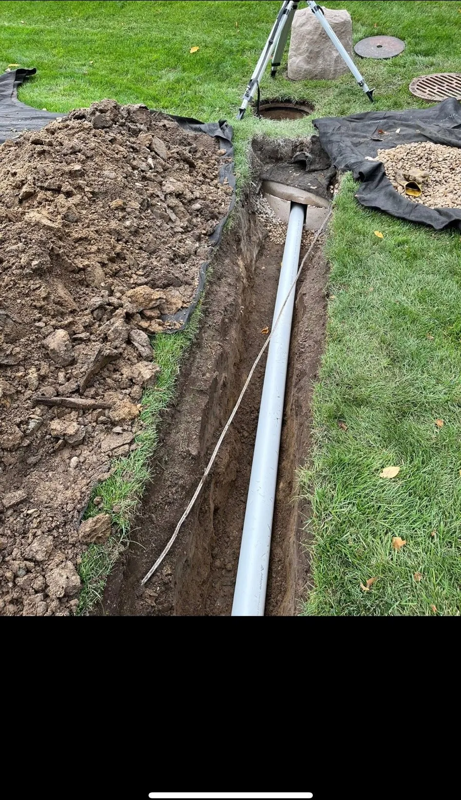 Drain line trenched across a lawn and tied into a manhole, set with a laser level